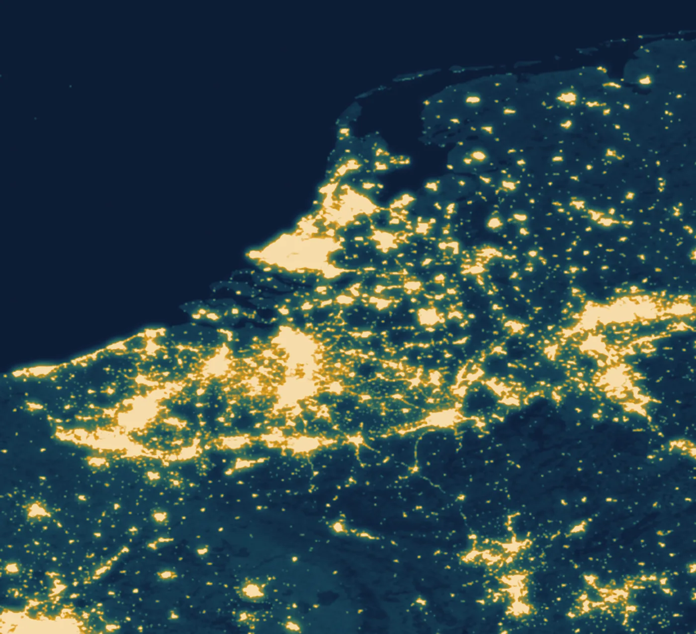 De Benelux gezien vanuit de ruimte bij nacht. De Randstad, de as Antwerpen–Brussel–Luik en de rand van het Ruhrgebied lichten okergoud op; de Ardennen, Zeeland en de Noordzee blijven donkerblauw.